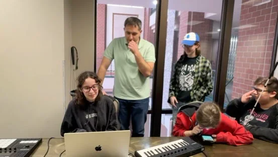 Blind students and instructors gather around a laptop and music keyboard during an accessible audio-technology exploration.