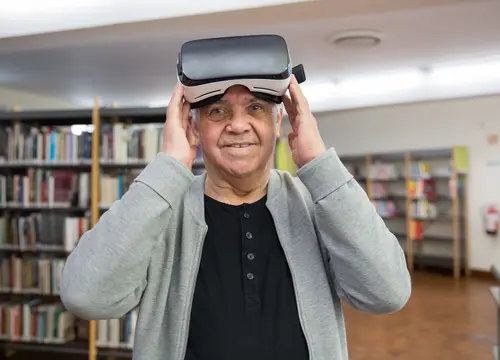 An older man explores virtual reality with a headset in a library.