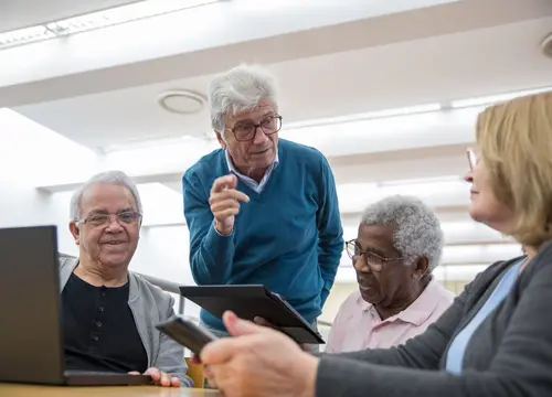 A diverse group of older adults learn together using a tablet and laptop.