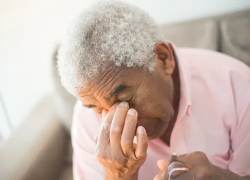 An older Black woman removes her glasses and rests a hand near her eye.