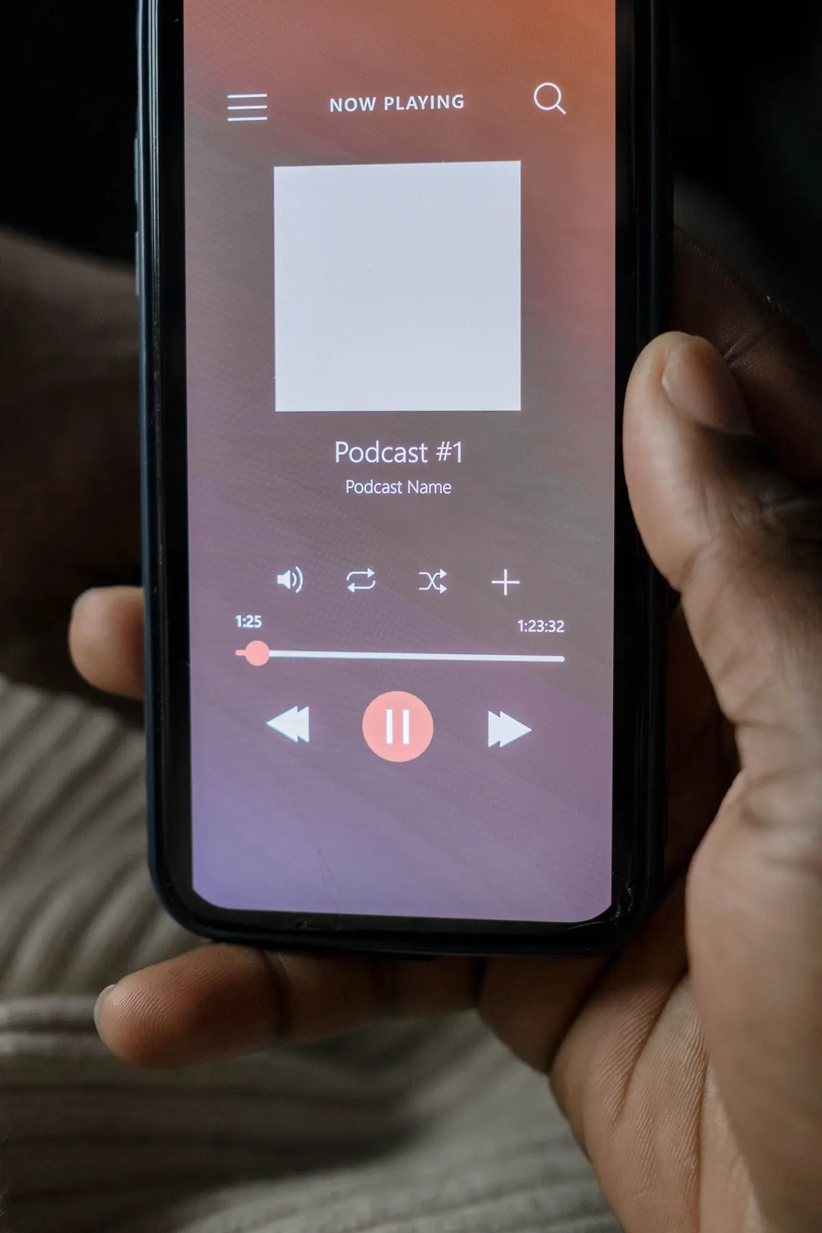 A hand holds a smartphone displaying a podcast playback screen with pause and navigation controls.