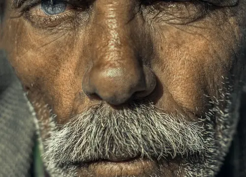 Close-up portrait of an older man’s eyes, weathered face, and gray beard.